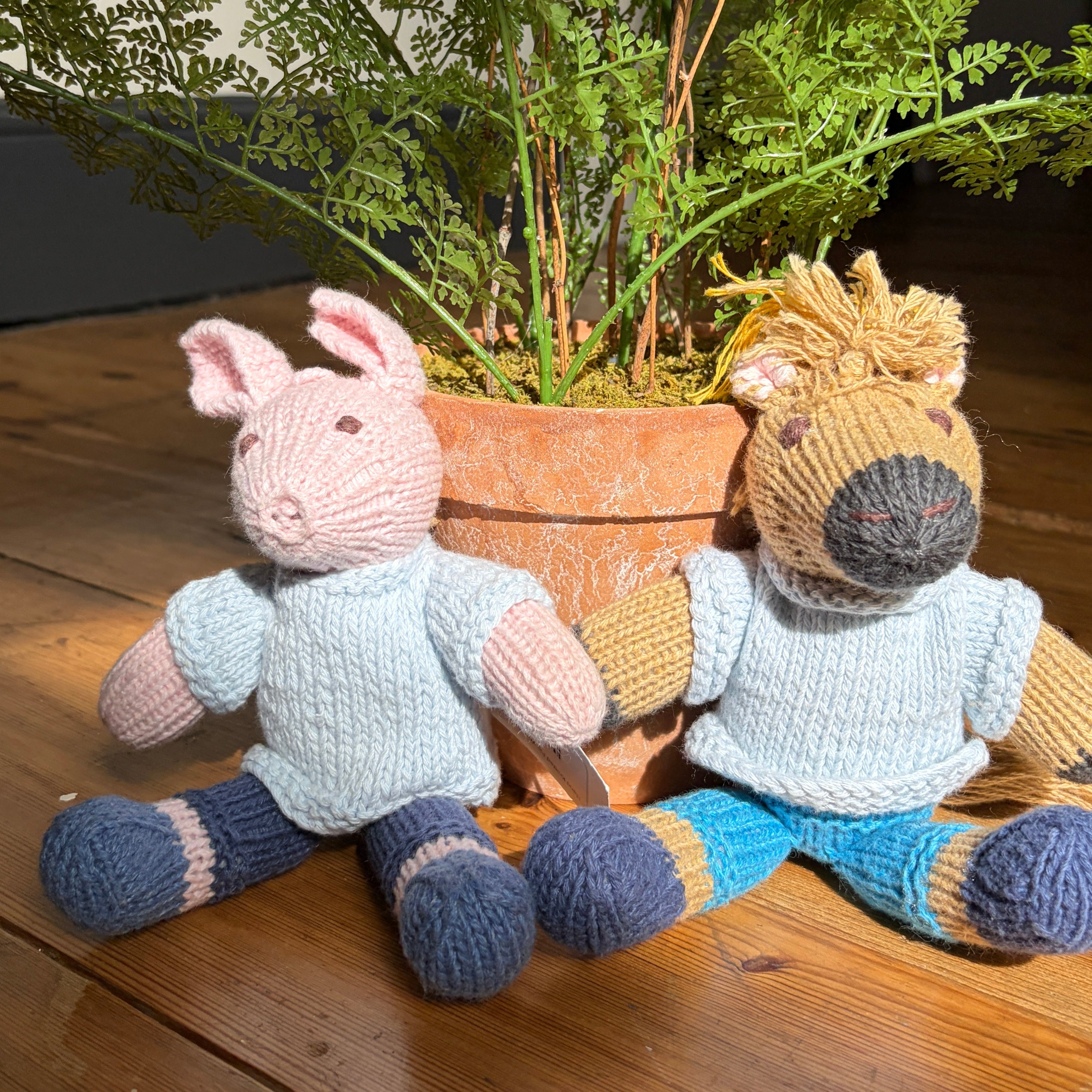 Two hand-knit stuffed animal toys sitting in front of a potted fern